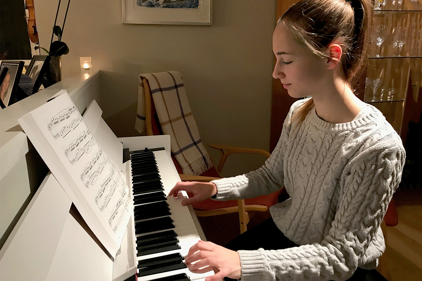 14-åriga Ella Carlstedt, i ljus tröja och hästsvans, sitter vid pianot i vardagsrummet hemma.