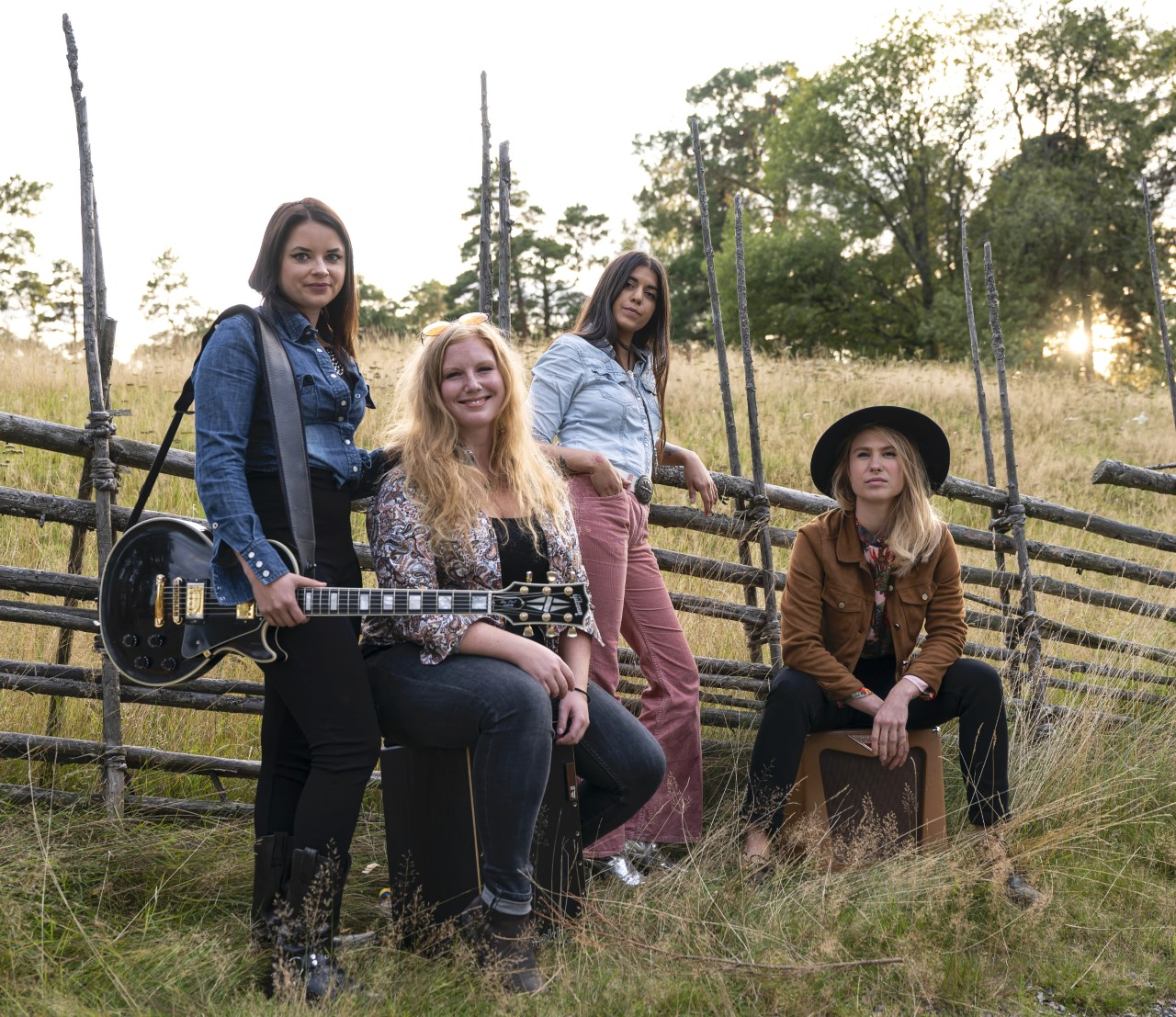 En bild på fyra kvinnor på ett fält. En håller i en gitarr, alla tittar mot kameran