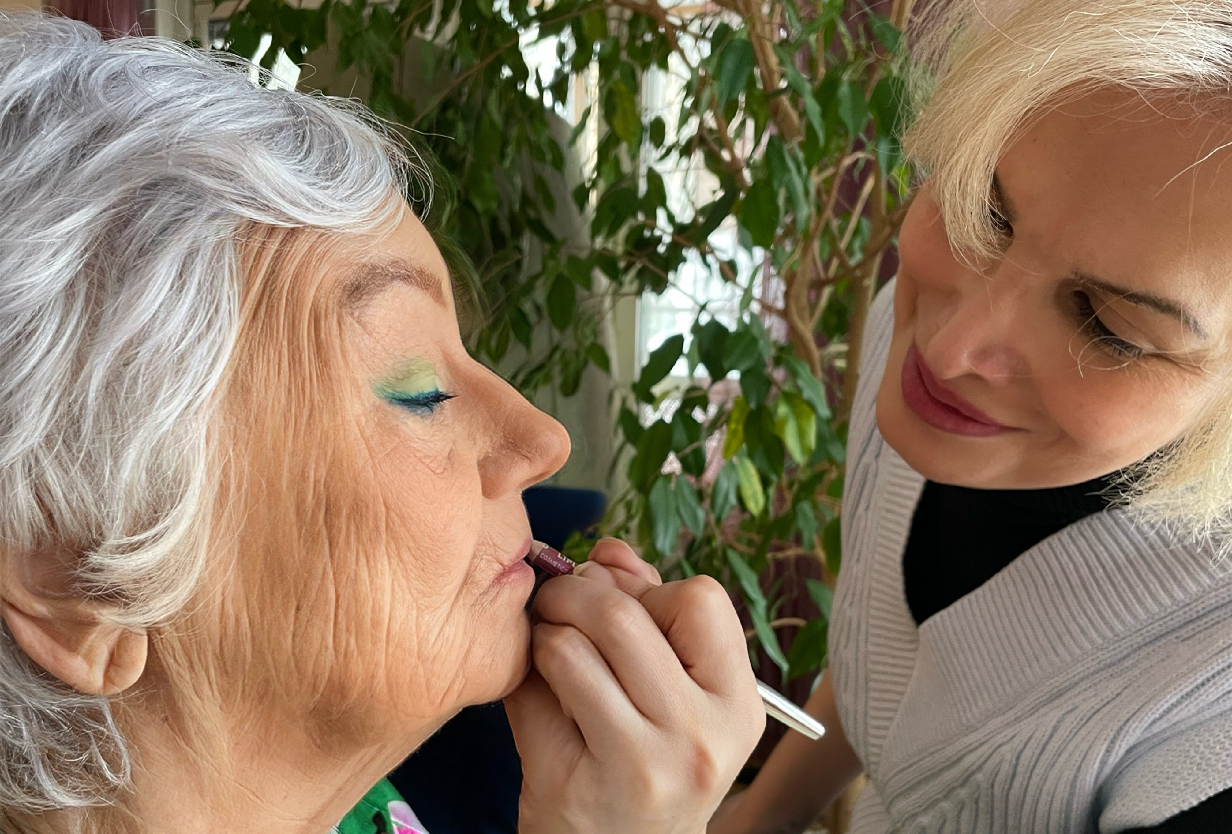 En äldre dam som får läppstift påmålat av en yngre kvinna