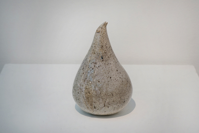 En glaserad keramikskulptur föreställande en gråfläckig fågelkropp med ett litet huvud och en liten näbb på toppen