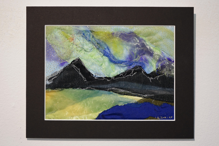 En tavla i olika material föreställande en horisont med svarta berg mot flerfärgade himmelsslöjor