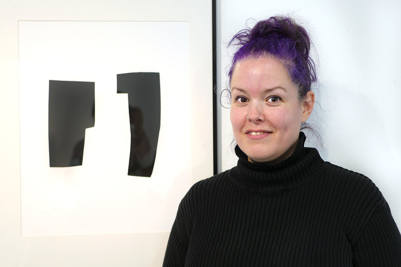 Meggi Sandell med lila hår och svart tröja framför en grafik ur serien Allt det viktiga.