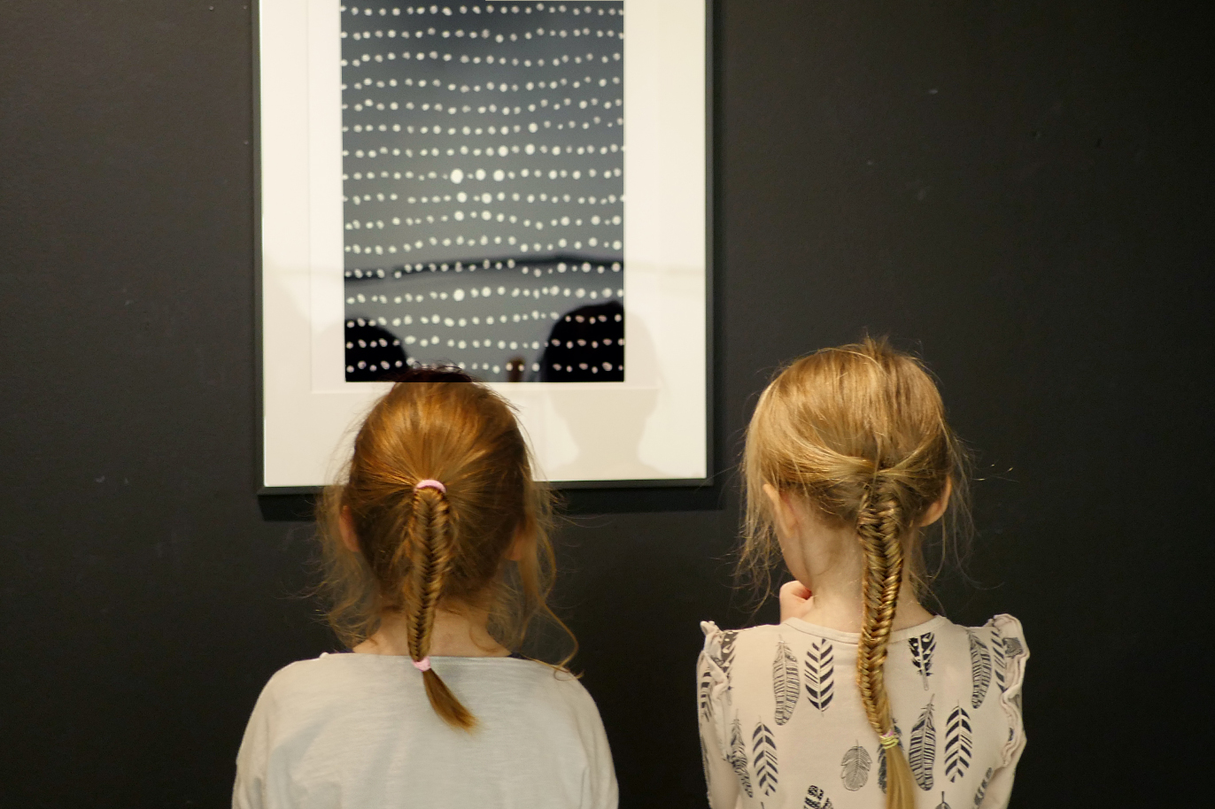 Två blonda flickor med flätor står och tittar på en grafik med vita prickar på svart botten.