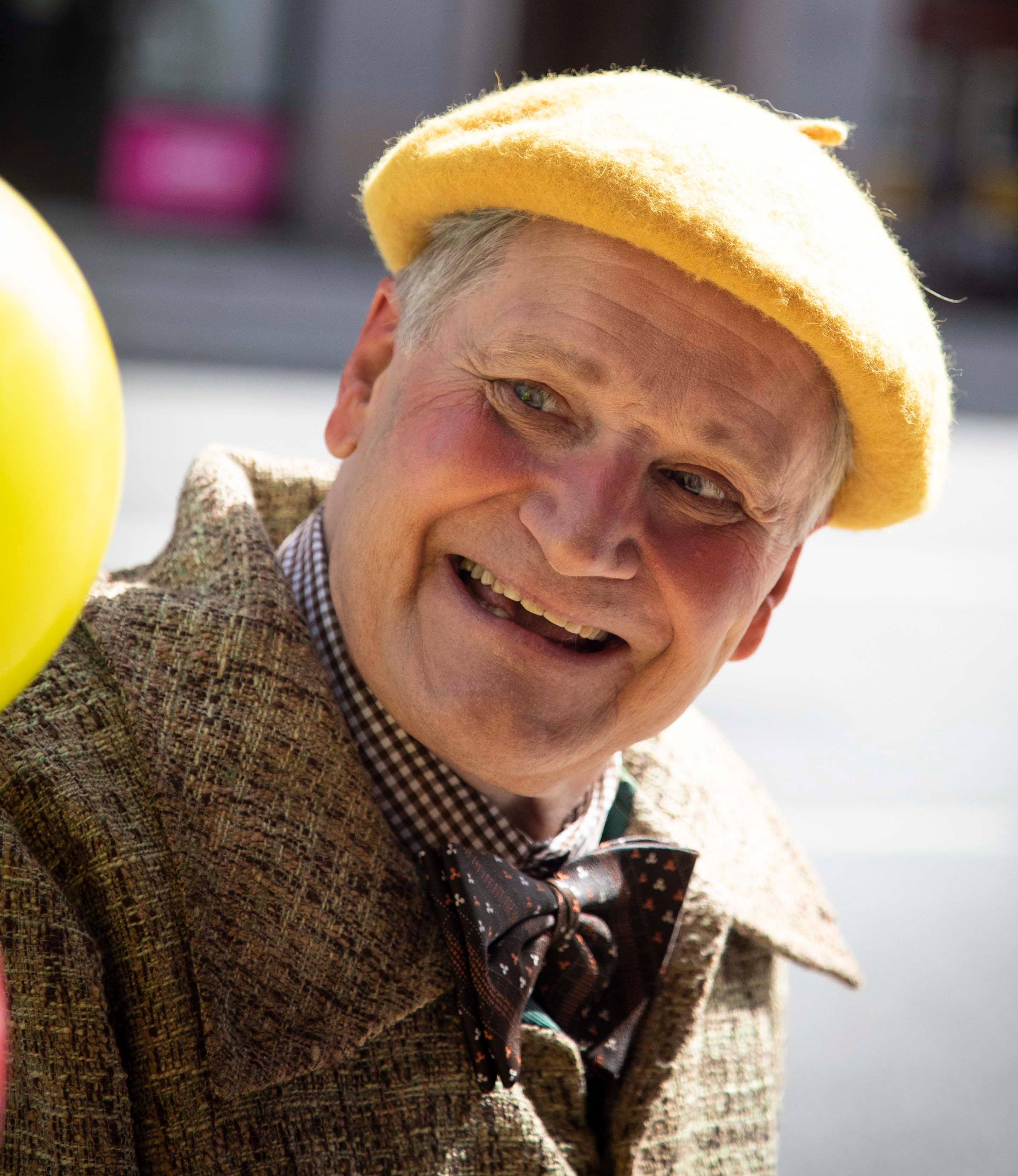 En man med gul basker tittar glatt på sin gula ballong.