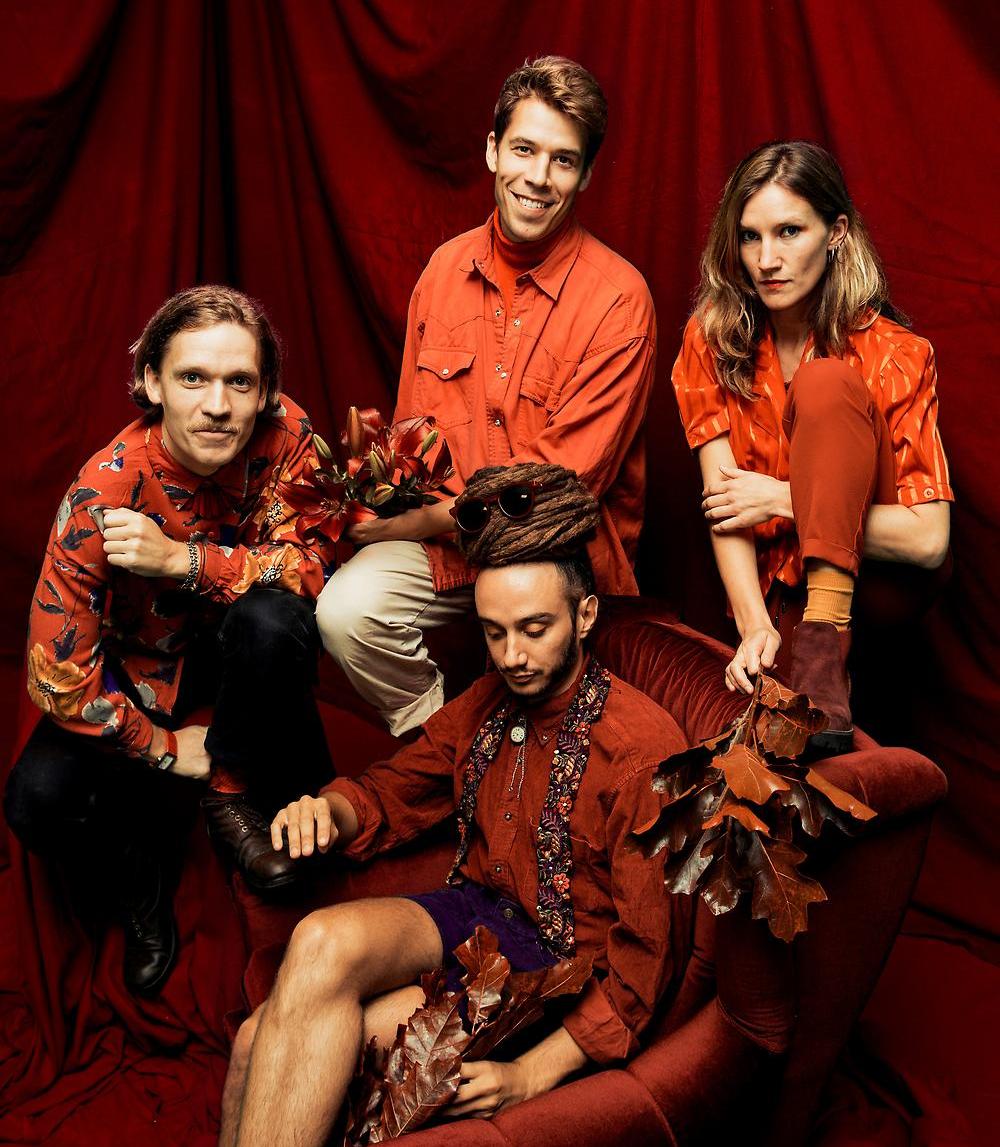 En bild på hela musikgruppen Kolonien med kläder och möbler i orangebruna toner.