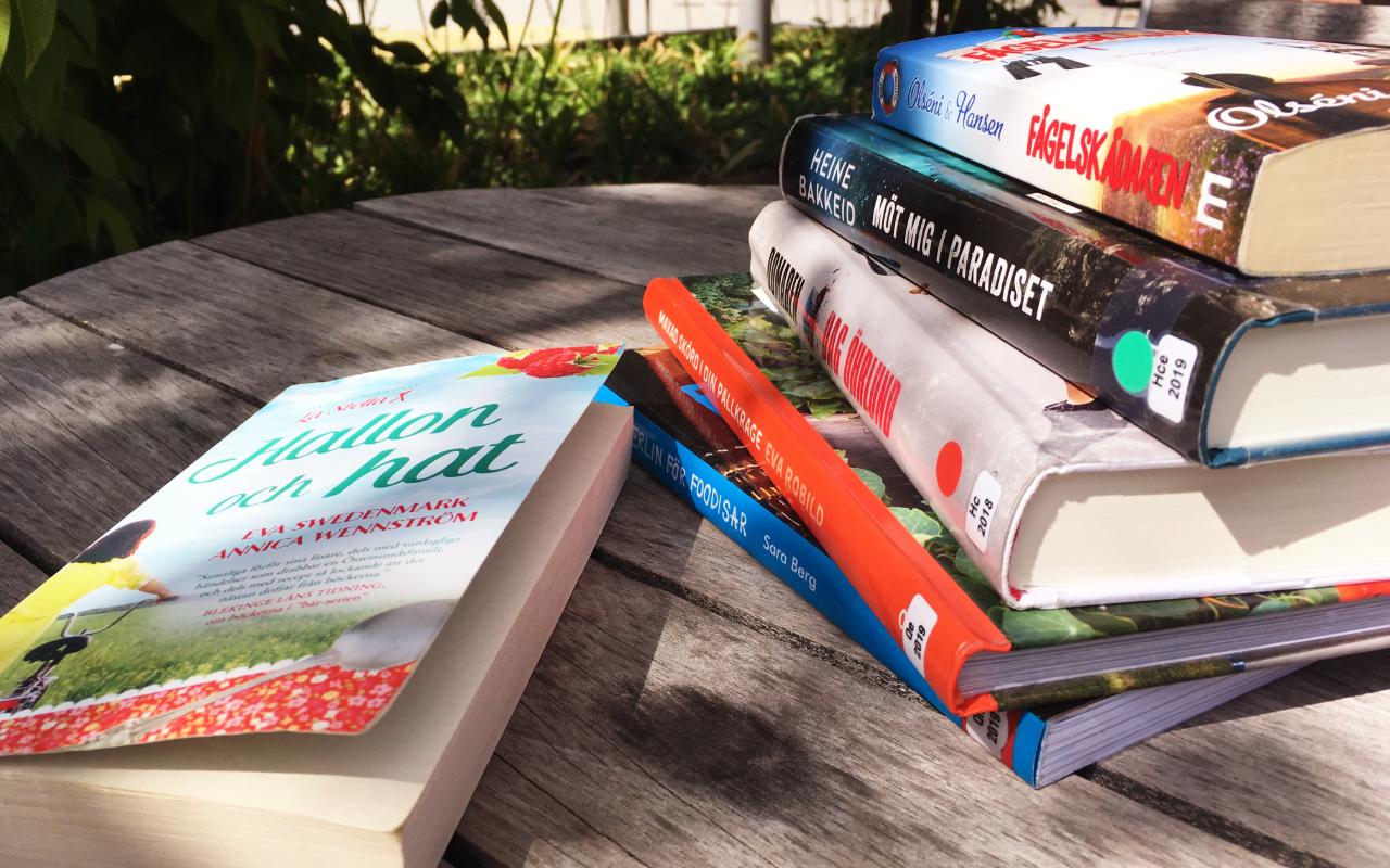 En hög med böcker ligger på ett bord ute i sommarsolen.